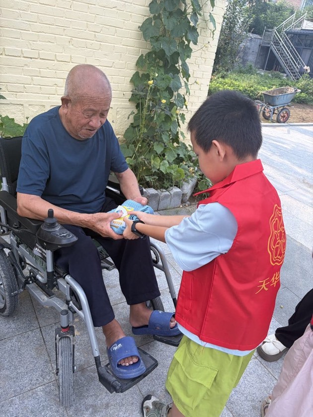 少年志愿者向轮椅上的长者递送慰问品